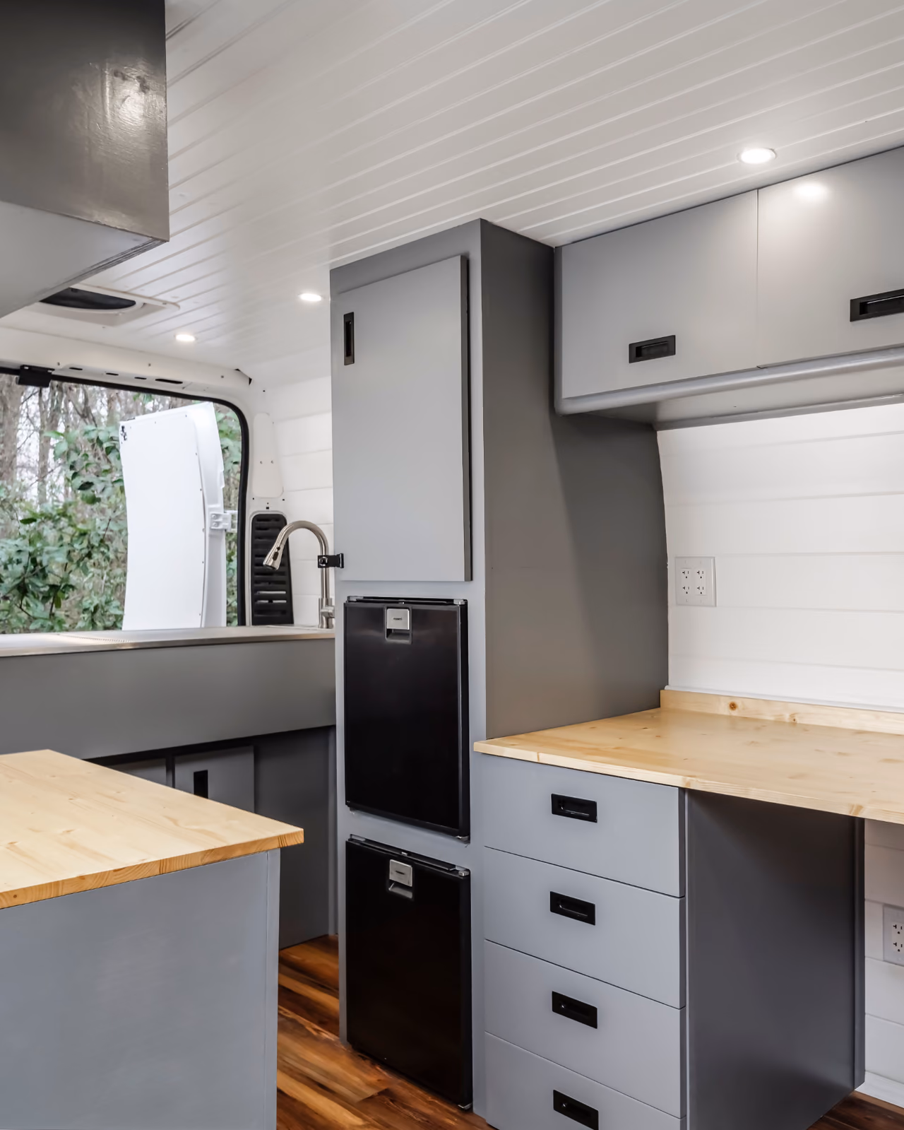 Finished mobile veterinary clinic interior with gray cabinetry, wood work surfaces, refrigeration, a sink, and overhead lighting.