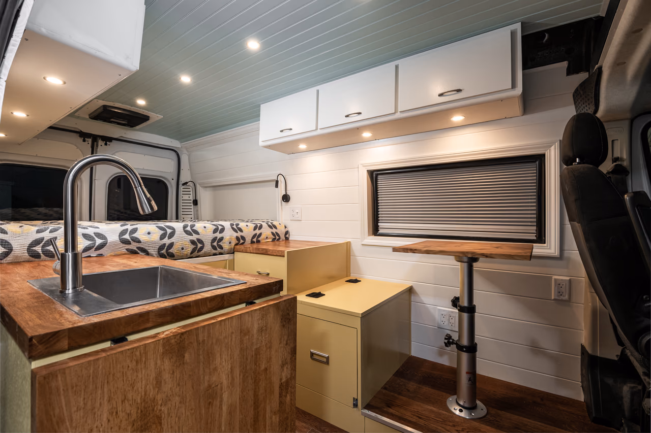 Completed campervan interior with a wood countertop, sink, rear bed, and seating area